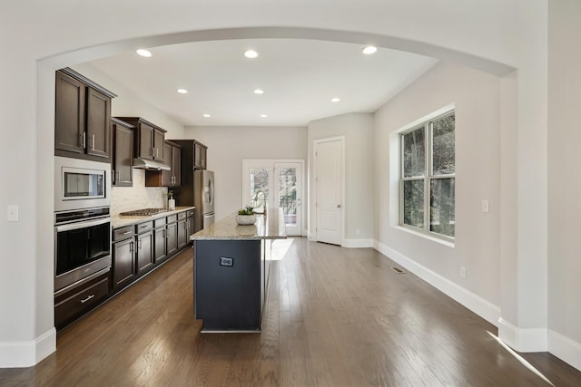 kitchen with arched walkways, stainless steel appliances, dark wood-style flooring, baseboards, and tasteful backsplash