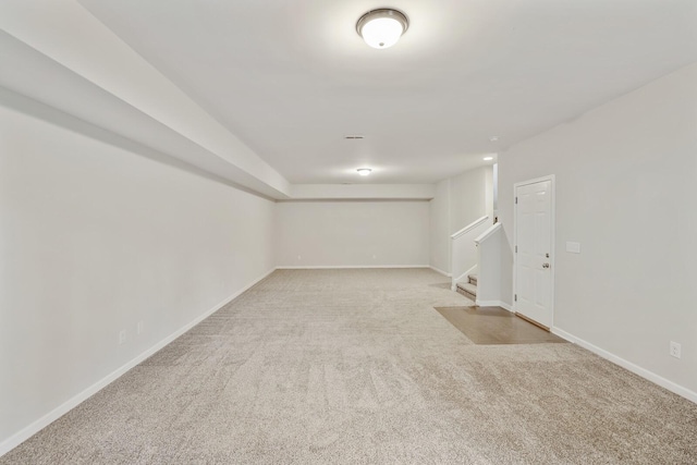 finished basement featuring stairs, baseboards, and light colored carpet