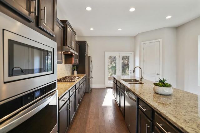 kitchen with stainless steel appliances, tasteful backsplash, a sink, dark brown cabinetry, and under cabinet range hood