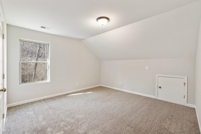 additional living space with carpet floors, visible vents, vaulted ceiling, and baseboards