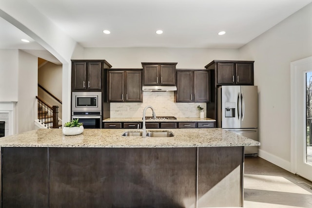 kitchen featuring decorative backsplash, appliances with stainless steel finishes, dark brown cabinets, under cabinet range hood, and a sink