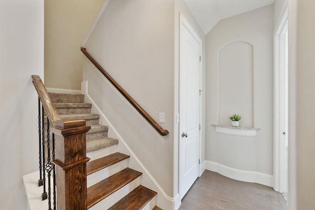 stairway featuring vaulted ceiling, wood finished floors, and baseboards