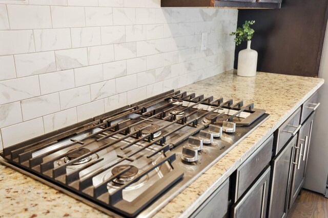 interior details featuring stainless steel gas stovetop, light stone counters, and backsplash