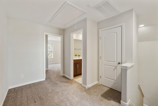 hall with light carpet, visible vents, attic access, and baseboards