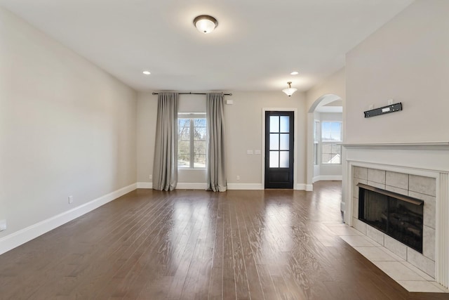 unfurnished living room featuring dark wood-type flooring, a tiled fireplace, and baseboards