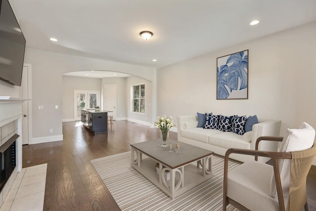 living area with recessed lighting, arched walkways, dark wood-style flooring, and a tile fireplace