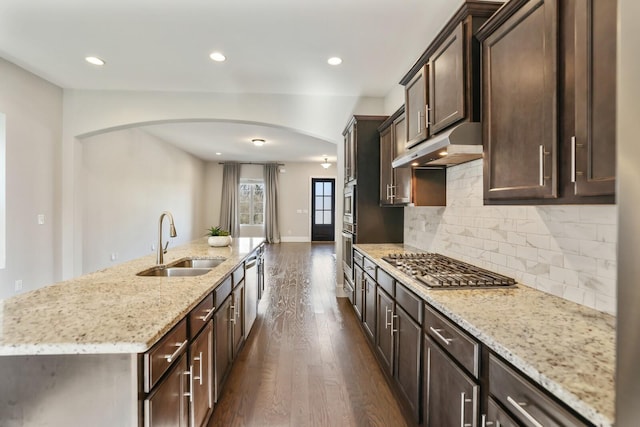 kitchen with arched walkways, under cabinet range hood, stainless steel appliances, dark wood-style flooring, and a sink