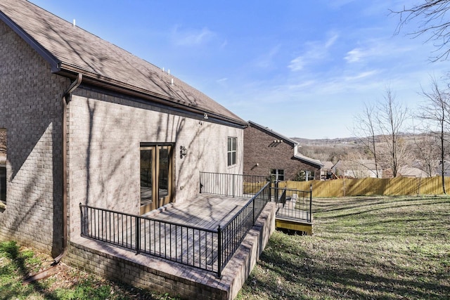 back of property with a deck, brick siding, a shingled roof, and fence