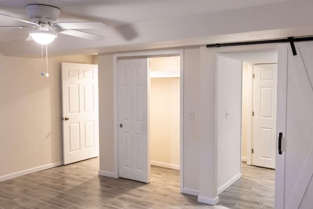 interior space featuring a ceiling fan, wood finish floors, baseboards, and a barn door