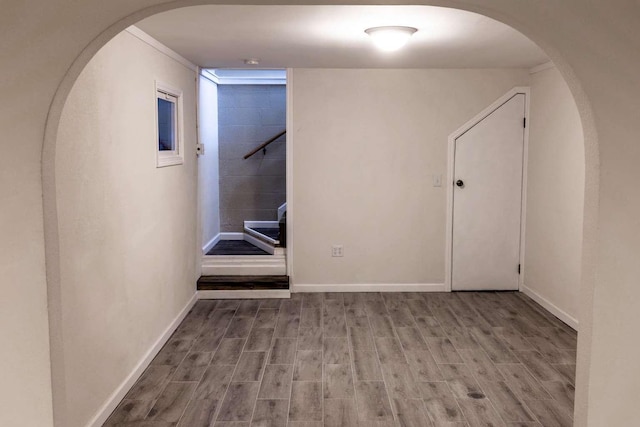 corridor featuring arched walkways, stairway, wood finished floors, and baseboards