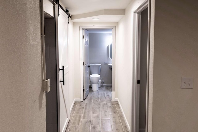 corridor with a barn door, wood finish floors, and baseboards