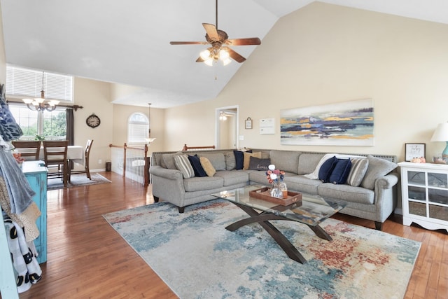 living area featuring baseboards, high vaulted ceiling, wood finished floors, and ceiling fan with notable chandelier