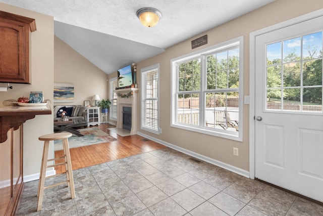 interior space featuring vaulted ceiling, light tile patterned floors, a fireplace with flush hearth, and a wealth of natural light