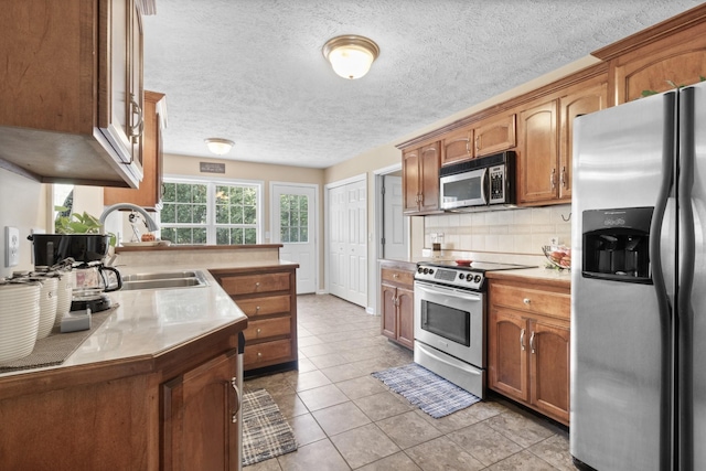 kitchen with light tile patterned floors, light countertops, appliances with stainless steel finishes, backsplash, and brown cabinetry