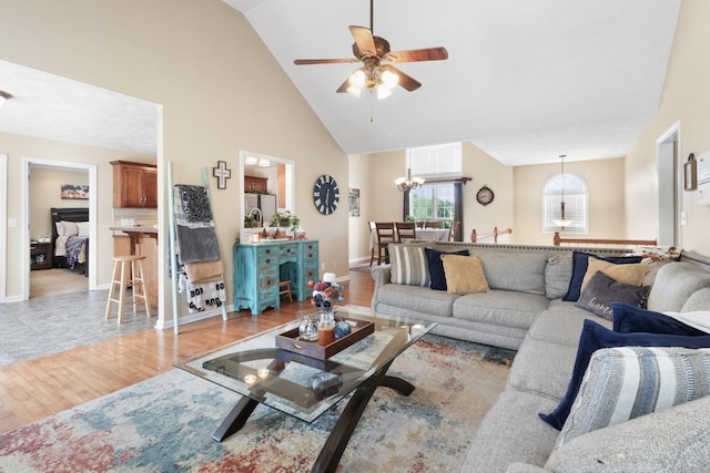 living room with light wood-style floors, baseboards, high vaulted ceiling, and ceiling fan with notable chandelier