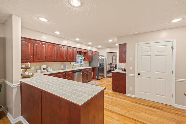 kitchen with tile countertops, stainless steel appliances, recessed lighting, light wood-style flooring, and a peninsula