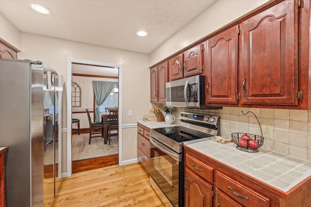 kitchen featuring light wood-style floors, appliances with stainless steel finishes, backsplash, and tile counters