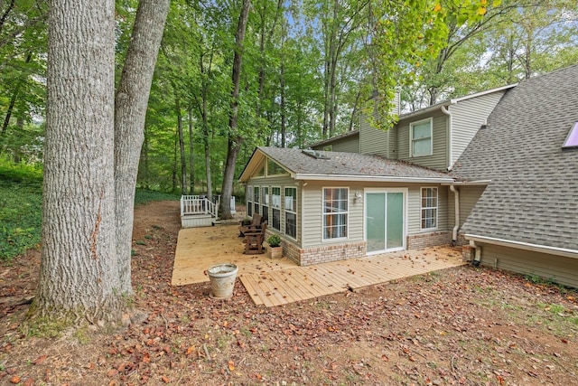 back of property featuring a deck, a sunroom, a shingled roof, and brick siding