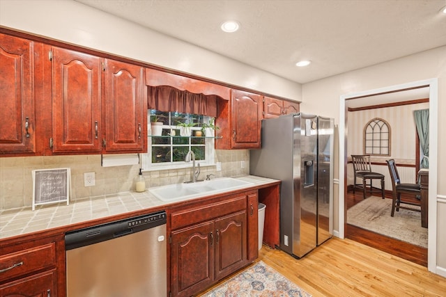 kitchen featuring a sink, appliances with stainless steel finishes, light wood-type flooring, tile counters, and tasteful backsplash