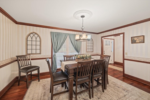 dining space featuring wallpapered walls, ornamental molding, wood finished floors, and wainscoting