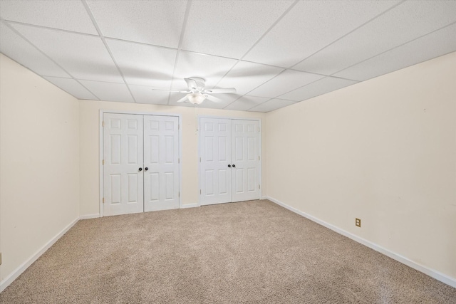 unfurnished bedroom featuring a paneled ceiling, baseboards, carpet floors, and two closets