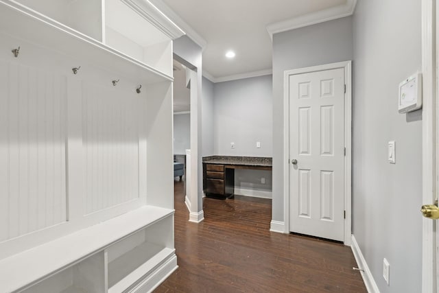 mudroom with dark wood finished floors, crown molding, built in desk, and baseboards