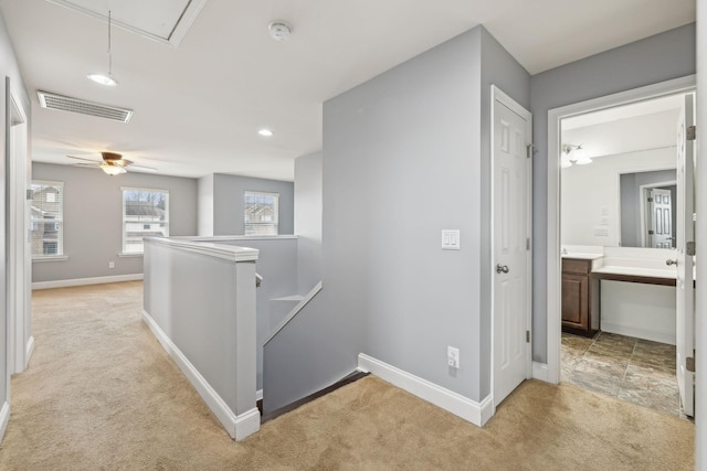 hallway with light carpet, visible vents, baseboards, an upstairs landing, and attic access