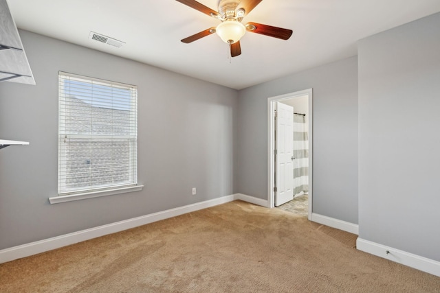 spare room with light carpet, ceiling fan, visible vents, and baseboards