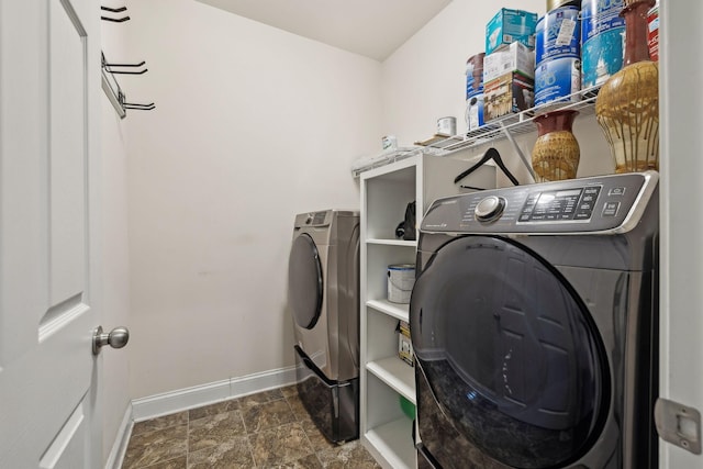 washroom featuring stone finish floor, laundry area, washing machine and dryer, and baseboards