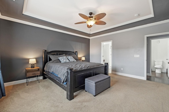 bedroom featuring a tray ceiling, light colored carpet, baseboards, and ensuite bathroom