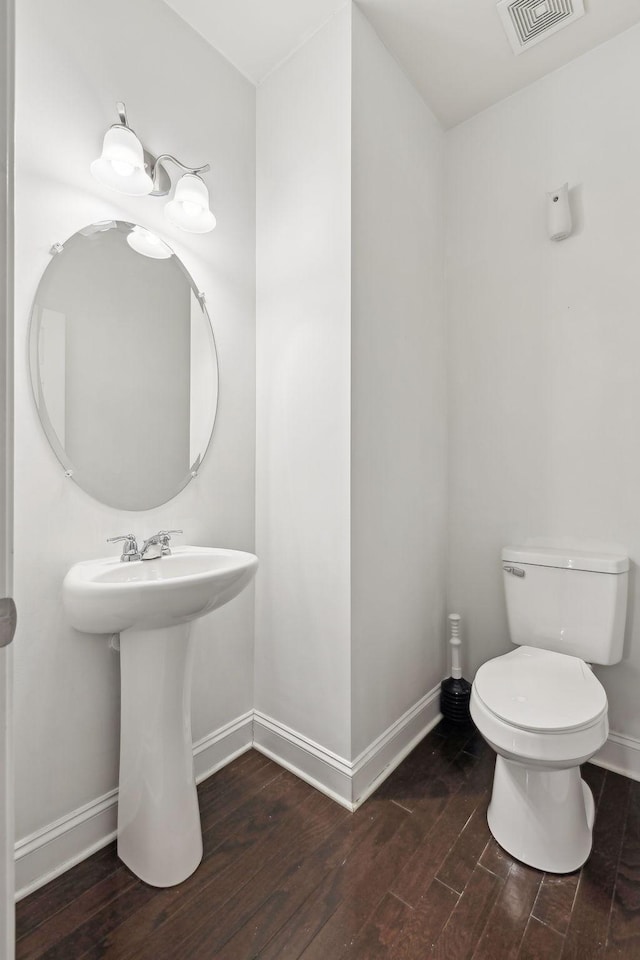 half bath with visible vents, toilet, baseboards, and wood finished floors