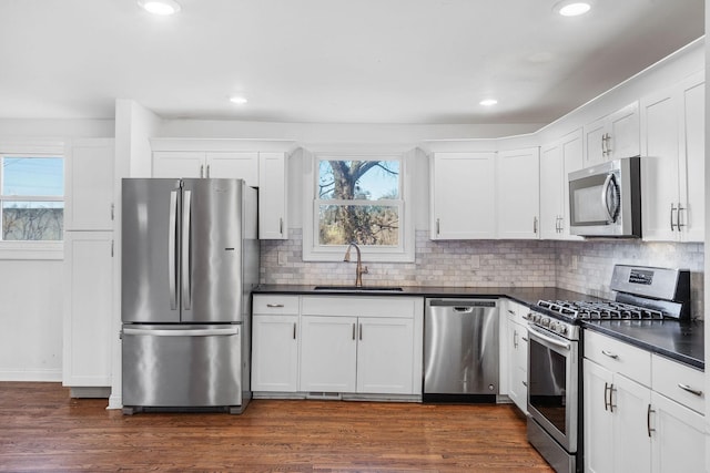 kitchen with stainless steel appliances, dark countertops, white cabinetry, and a sink