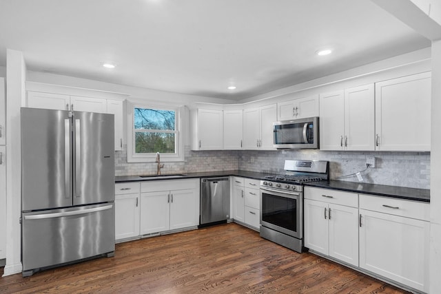 kitchen with white cabinets, dark countertops, appliances with stainless steel finishes, dark wood-type flooring, and a sink