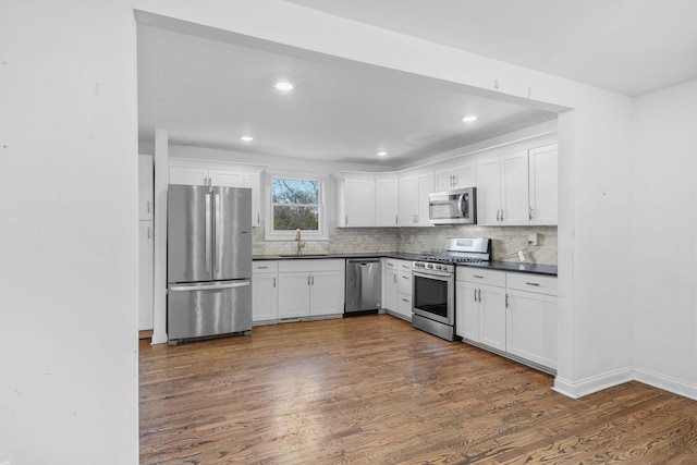 kitchen featuring stainless steel appliances, dark countertops, dark wood-type flooring, and a sink