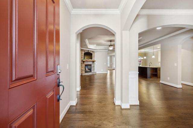 foyer with ornamental molding, dark wood-type flooring, a fireplace, and a ceiling fan