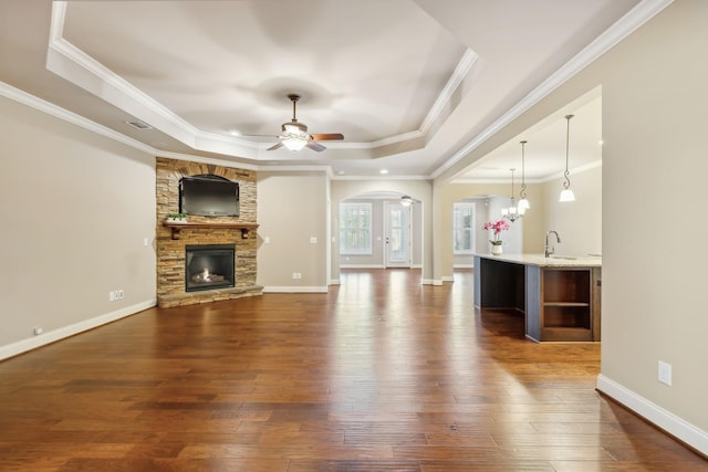 unfurnished living room with arched walkways, ceiling fan with notable chandelier, a fireplace, dark wood finished floors, and a raised ceiling