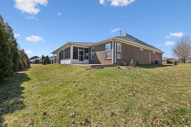 back of house with central air condition unit, a sunroom, a lawn, and brick siding