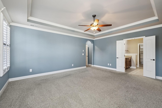 unfurnished room featuring arched walkways, ceiling fan, a tray ceiling, and light carpet