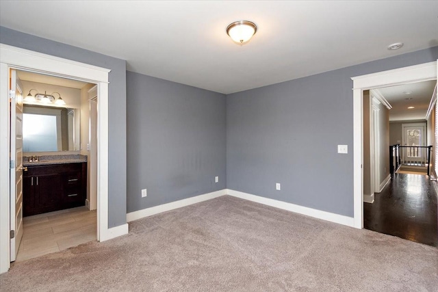 unfurnished bedroom featuring baseboards, ensuite bath, a sink, and light colored carpet