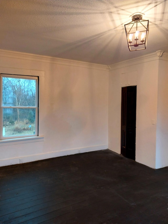 spare room with a textured ceiling, ornamental molding, dark wood finished floors, and an inviting chandelier