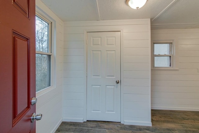 foyer with dark wood-style floors, wooden walls, and baseboards