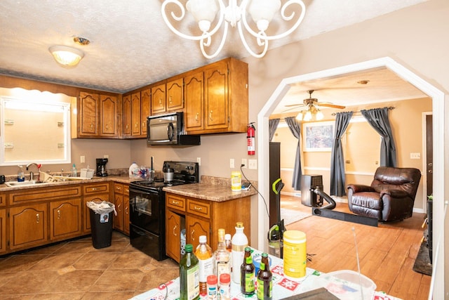 kitchen with a textured ceiling, a sink, light countertops, black appliances, and brown cabinetry