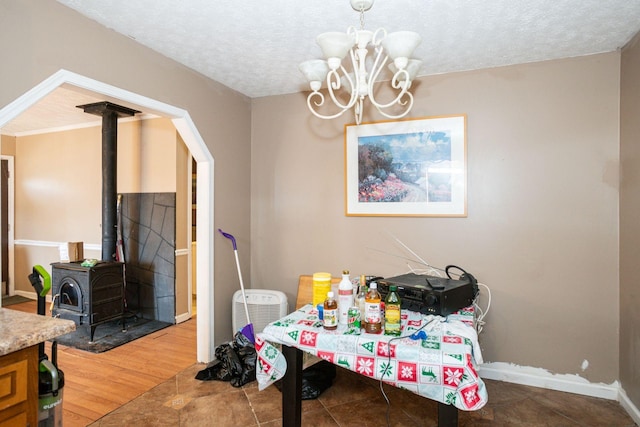 dining space with a notable chandelier, a wood stove, a textured ceiling, wood finished floors, and baseboards