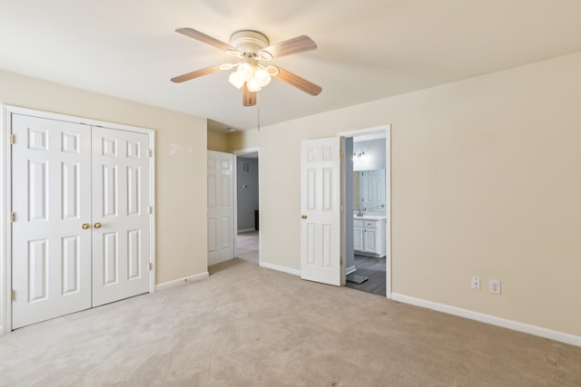 unfurnished bedroom featuring light carpet, baseboards, ceiling fan, ensuite bathroom, and a closet