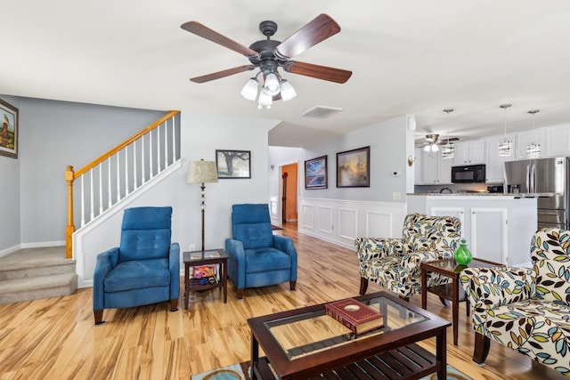 living area with visible vents, a decorative wall, light wood-style floors, a ceiling fan, and stairs