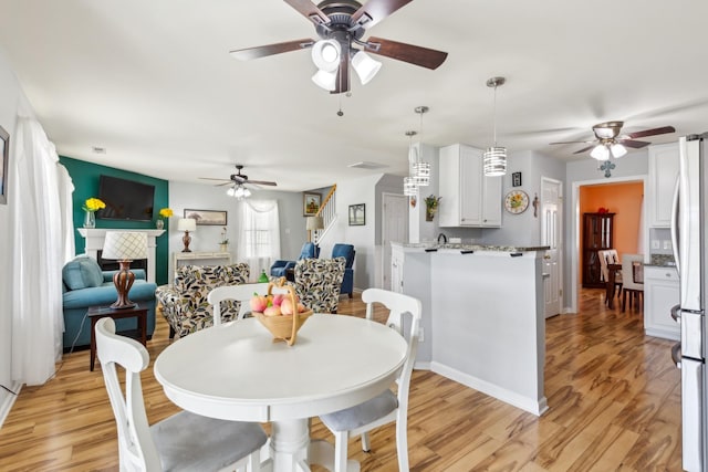 dining room featuring light wood-type flooring, ceiling fan, baseboards, and a tiled fireplace