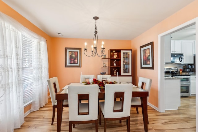 dining room with light wood-type flooring, baseboards, visible vents, and a notable chandelier