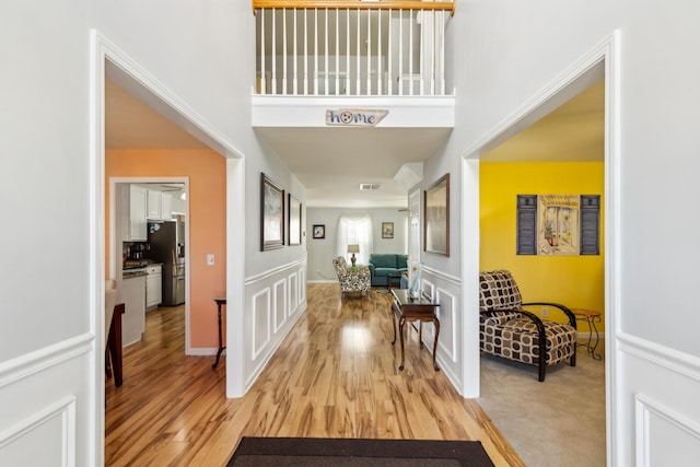 corridor featuring visible vents, light wood finished floors, and a high ceiling