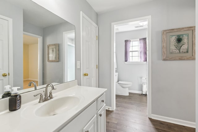 bathroom with visible vents, toilet, vanity, wood finished floors, and baseboards