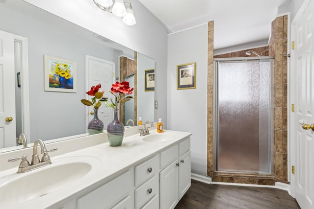 bathroom with double vanity, a shower stall, a sink, and wood finished floors